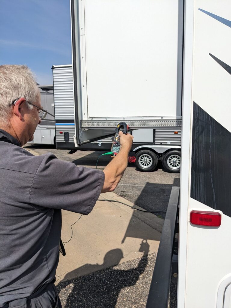 A gray haired man in a charcoal shirt and shorts performs an RV inspection using a RV inspection report software on a mobile app